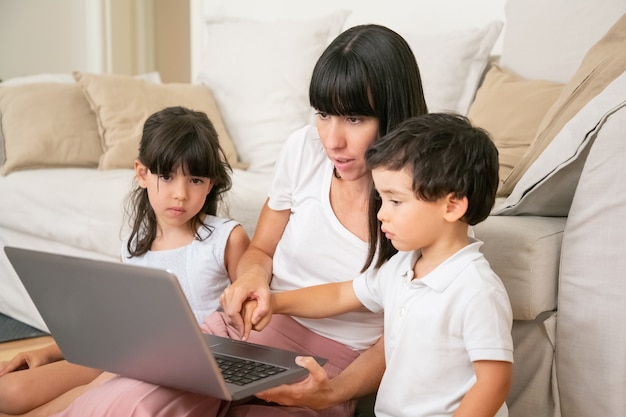 Maman apprend aux enfants à utiliser un ordinateur portable, tenant la main du petit fils et en appuyant sur le bouton du clavier avec le doigt du garçon.