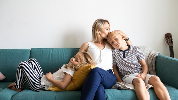Maman blonde embrasse la tête de son fils et se détend avec sa fille sur le canapé