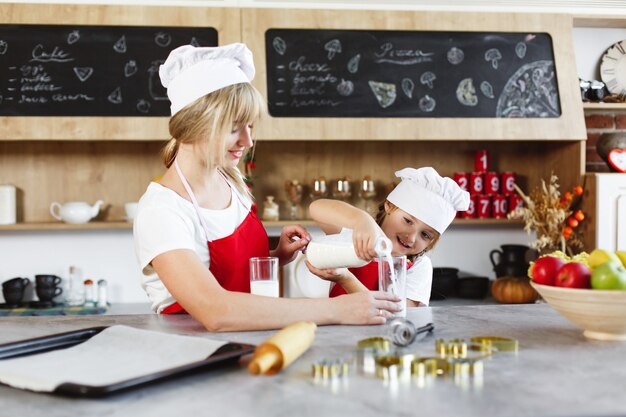 Maman et charmante petite fille s’amusent à boire du lait à la table dans une cuisine chaleureuse