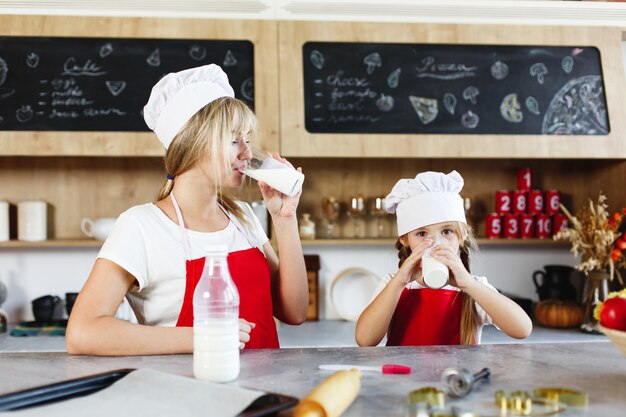 Maman et charmante petite fille s’amusent à boire du lait à la table dans une cuisine chaleureuse
