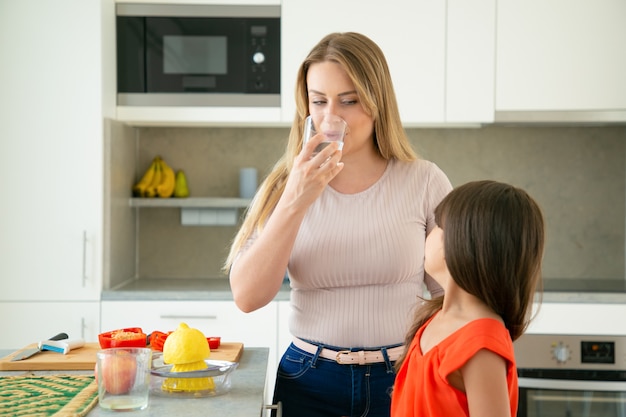 Maman et fille buvant de l'eau tout en pressant du jus de citron, cuire une salade ensemble dans la cuisine. Cuisine familiale ou concept de mode de vie sain