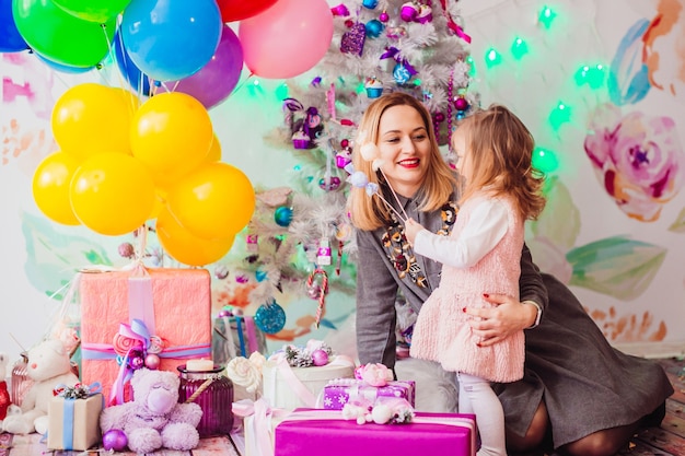 Maman et fille jouent devant un arbre de Noël dans une chambre rose