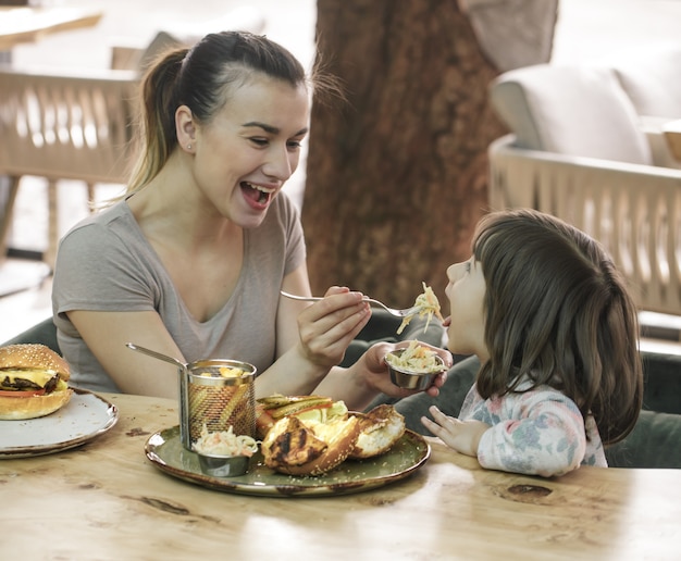 Maman avec une jolie fille mangeant de la restauration rapide dans un café