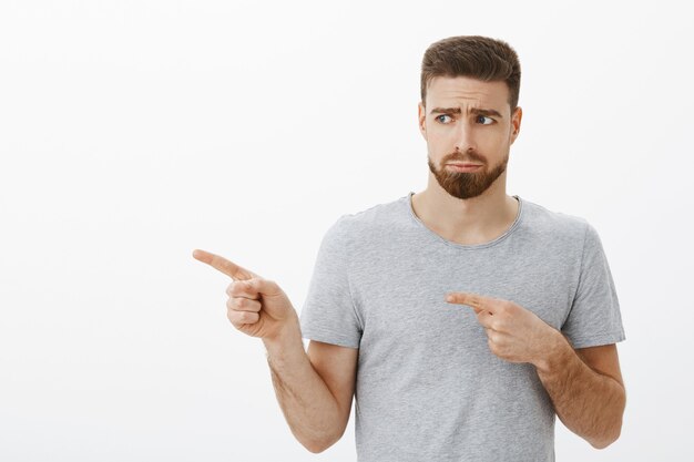 Maman, ce mec m'offense. Portrait de malheureux et triste masculin et beau mâle adulte barbu avec une coiffure cool fronçant les sourcils et faisant la moue de regret et d'envie pointant et regardant à gauche