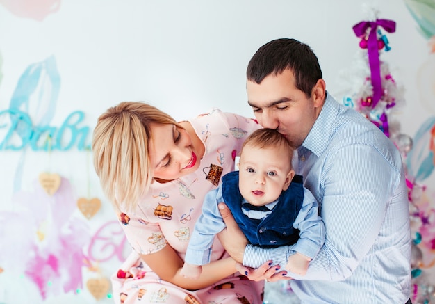 Maman, papa et leur petit fils posent dans la chambre avec un arbre de Noël rose