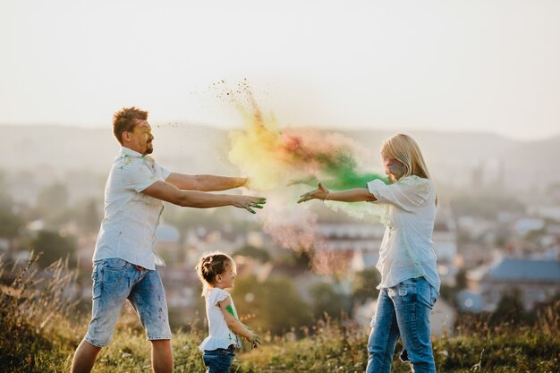 Maman et papa et leur petite fille jouent avec de la fumée colorée sur la pelouse