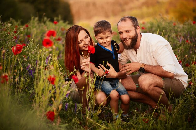 Maman et papa tiennent leur petit fils sur les bras debout sur le champ vert avec des coquelicots