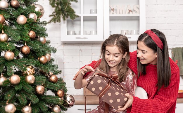 Maman avec une petite fille près de l'arbre de Noël avec une boîte-cadeau