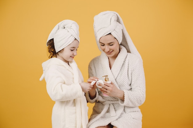 Maman avec sa fille. Filles avec des peignoirs blancs. Maman apprend à sa fille à se maquiller.