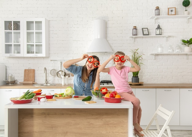 Maman et sa fille préparent une salade dans la cuisine. Amusez-vous et jouez avec les légumes