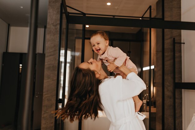 Maman et sa fille s'amusent dans leurs appartements élégants. Portrait de dame aux cheveux longs tenant enfant riant.