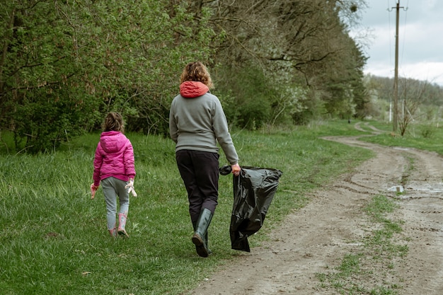 Maman et sa fille avec des sacs poubelle nettoient l'environnement des ordures.