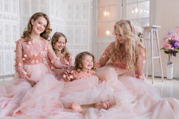 Maman et ses trois filles vêtues de gawns roses posent dans une chambre blanche de luxe