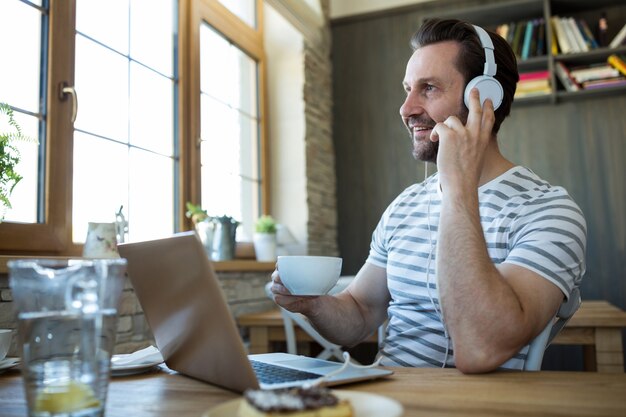 Man écoute au casque et la tenue d&#39;une tasse de café au café