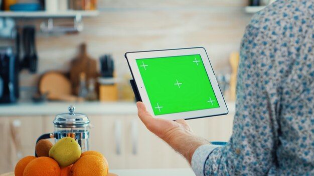 Man holding tablet pc avec clé chroma dans la cuisine pendant le petit déjeuner. Personne âgée avec une maquette isolée à écran vert pour un remplacement facile