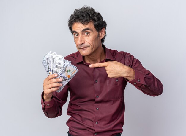 Man in purple shirt holding cash pointant avec l'index à l'argent à la surprise et heureux