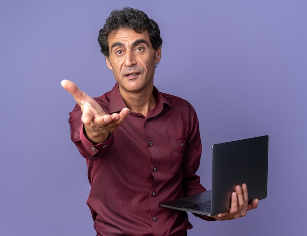 Photo gratuite man in purple shirt holding laptop looking at camera faisant venir ici geste