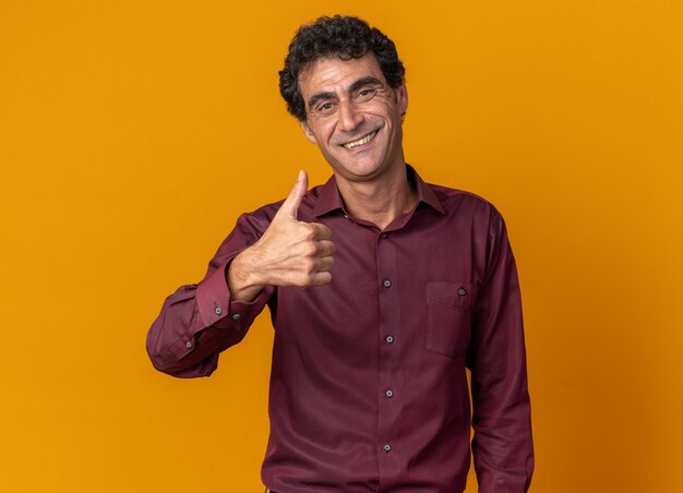 Man in purple shirt looking at camera smiling confiant showing Thumbs up