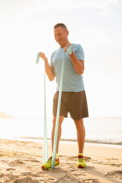 Man working out avec corde élastique sur la plage