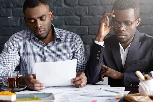 Manager afro-américain portant des lunettes et son collègue ayant l'air fatigué et stressé