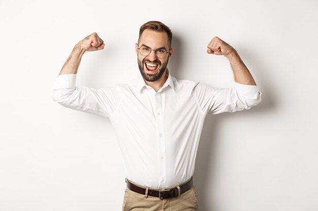 Le manager qui réussit fléchit les biceps, montre ses muscles et a l'air confiant, debout.