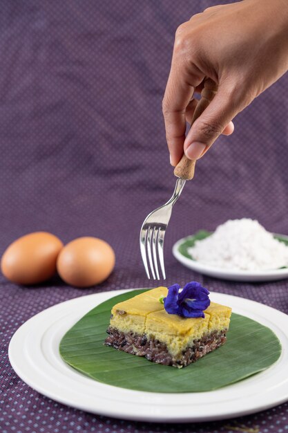 Le manche d'une fourchette qui s'apprête à insérer le dessert de riz gluant noir avec crème anglaise sur la feuille de bananier.