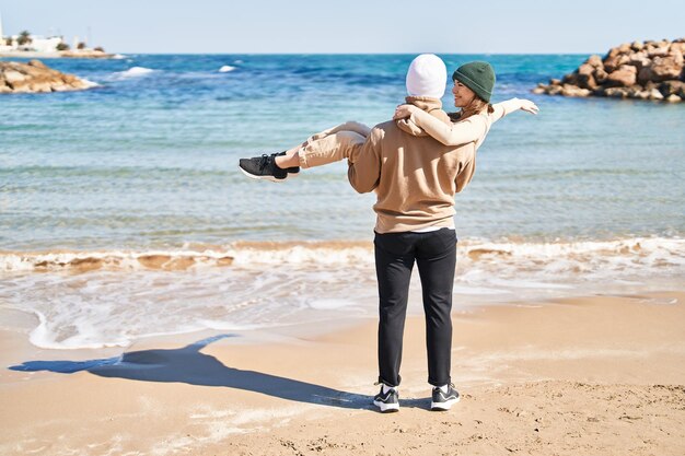 Mand et femme couple s'embrassant tenant petite amie sur les bras au bord de la mer