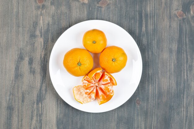 Mandarine épluchée avec des mandarines entières sur plaque blanche