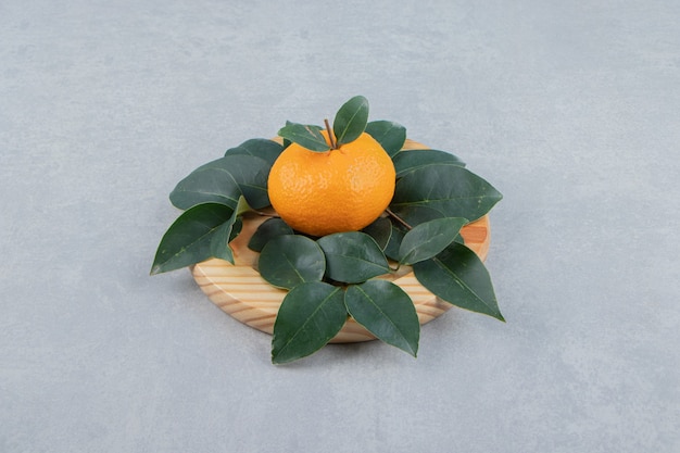 Photo gratuite mandarine fraîche unique avec des feuilles sur une plaque en bois