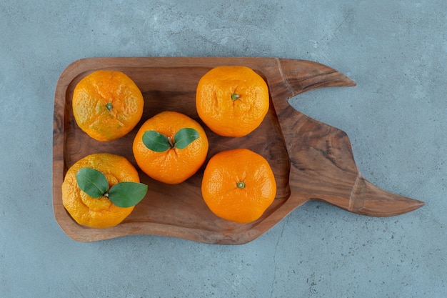 Mandarine et oranges sur un plateau en bois, sur fond de marbre.