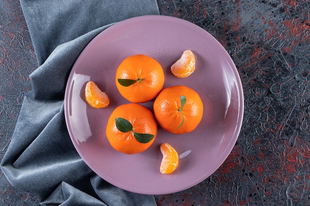 Photo gratuite mandarines mûres avec des feuilles placées sur une assiette violette