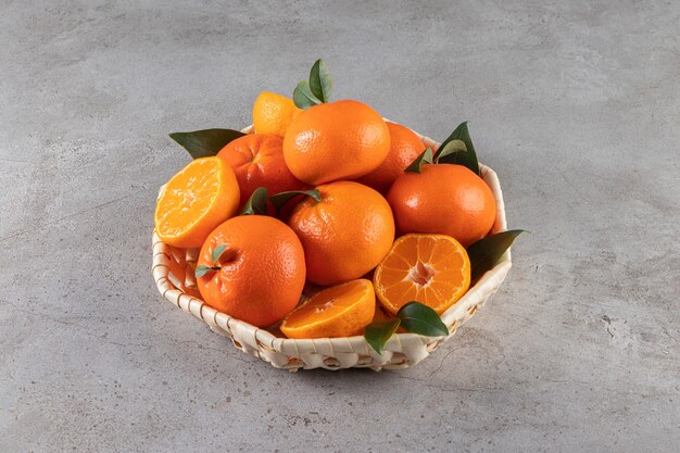 Mandarines mûres avec des feuilles placées dans un panier en osier sur la surface de la pierre