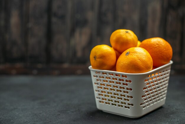 Mandarines et oranges vue de face dans un panier en plastique sur un espace libre sombre