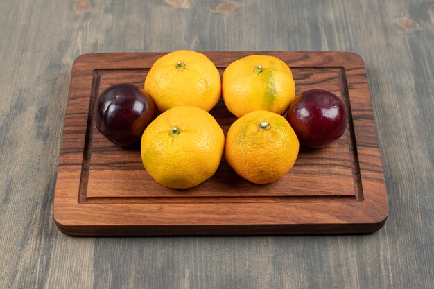 Mandarines sucrées aux prunes sur une planche à découper en bois. Photo de haute qualité