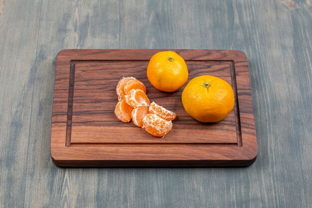 Mandarines tranchées et entières sur une planche à découper en bois