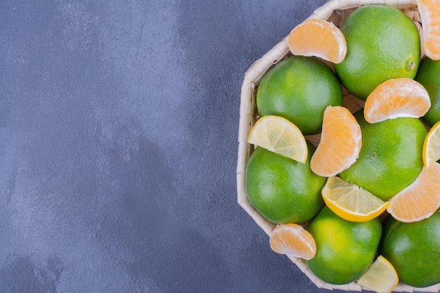 Mandarines vertes dans un panier en bambou sur table bleue.