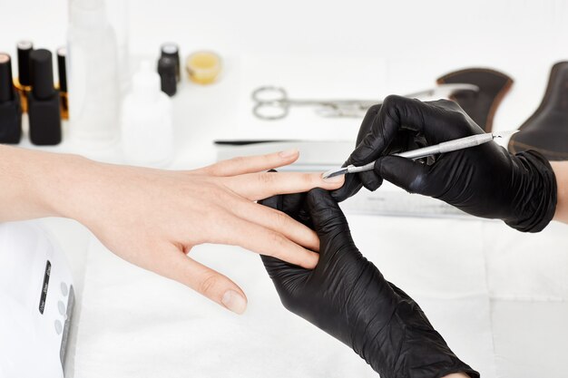 Manicrurist dans des gants poussant la cuticule sur l'annulaire de la femme.