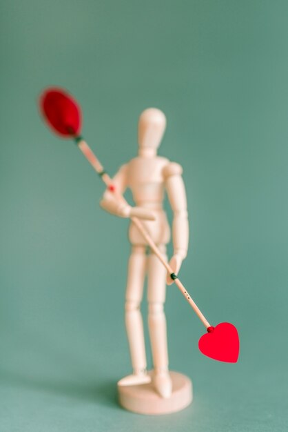 Mannequin en bois tenant une flèche d&#39;amour sur la table verte