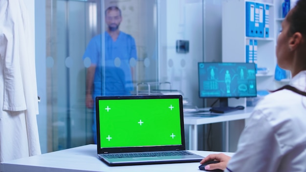 Maquette verte sur l'ordinateur portable du médecin à l'hôpital et l'infirmière ouvrant la porte vitrée de l'armoire.