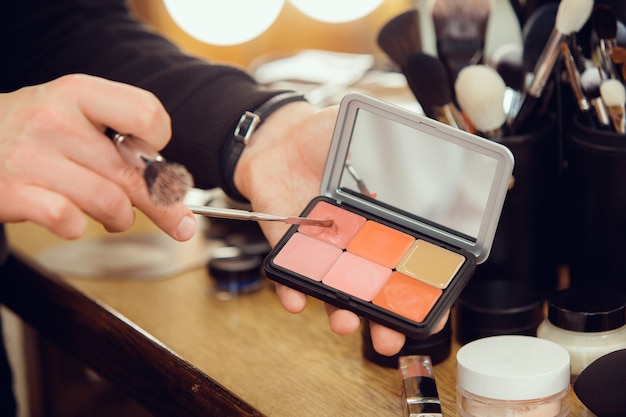 Maquilleuse professionnelle travaillant au salon. L'homme au proffesion féminine. Concept d'égalité des sexes. Mains mâles avec gros plan de brosse