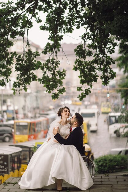 Marié sur un fauteuil roulant tient la mariée sur ses genoux assis dehors dans le parc