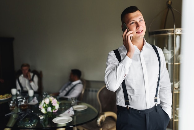 Le marié parle au téléphone debout devant une fenêtre dans la chambre