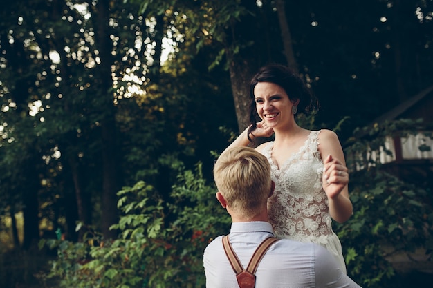 Le marié tient sa mariée dans ses bras quelque part dans la nature