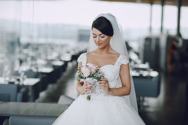 Une mariée élégante et belle dans une robe blanche et un voile debout avec bouquet de fleurs