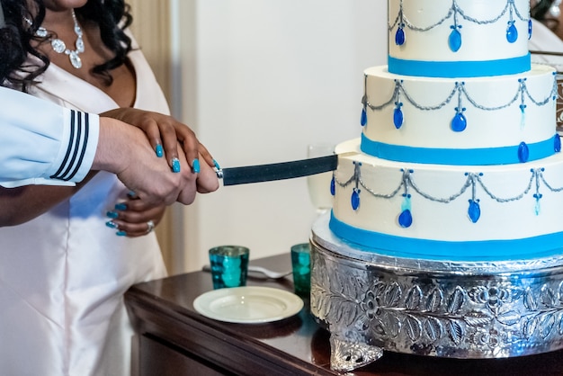 Photo gratuite mariée et un marié coupant le beau gâteau de mariage blanc - concept de mariage interracial