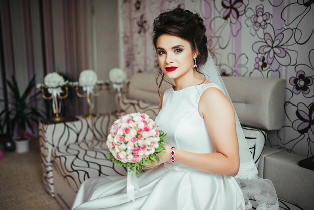 Mariée tenant un bouquet de mariée avec de petites roses jaunes et roses et en regardant à la caméra.