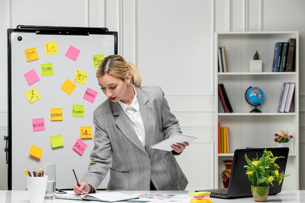 Marketing jolie jeune femme d'affaires en costume gris au bureau en train d'écrire des notes