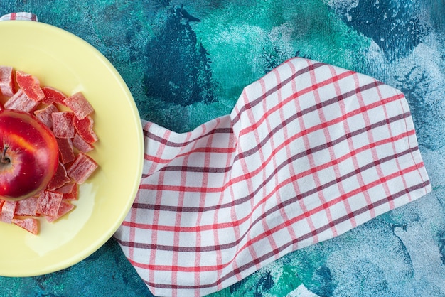 Photo gratuite marmelade rouge en tranches et pomme dans une assiette sur un torchon , sur la table bleue.