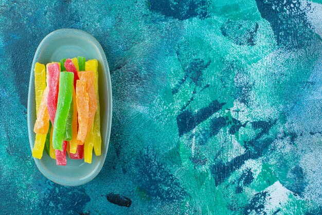 Marmelade sous forme de bâtonnets colorés dans une assiette sur bleu.