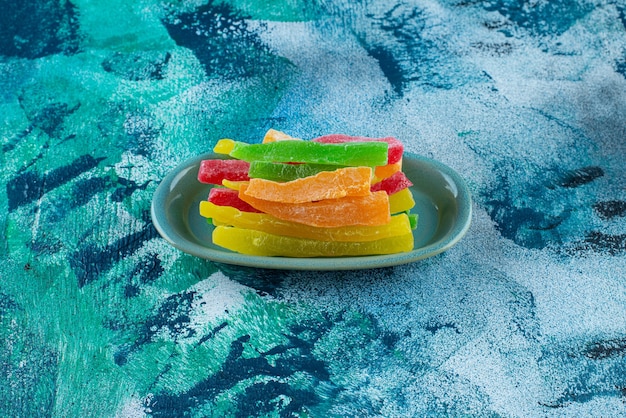 Marmelade sous forme de bâtonnets colorés dans une assiette, sur la table bleue.